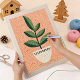 Hands using a punch needle kit to create a green-potted plant design on textured fabric.